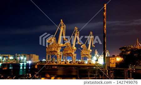 A grand, imposing night view of an industrial area, featuring giant cranes. A grand, imposing night view of an industrial area, featuring giant cranes. 142749076