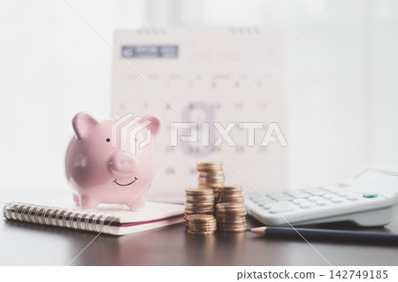 Pink piggy bank beside a calendar, calculator, notebook, pencil, and coin stacks represents monthly budgeting, savings planning, expense tracking, payment deadlines, and future financial goals. Pink piggy bank beside a calendar, calculator, notebook, pencil, and coin stacks represents monthly budgeting, savings planning, expense tracking, payment deadlines, and future financial goals. 142749185