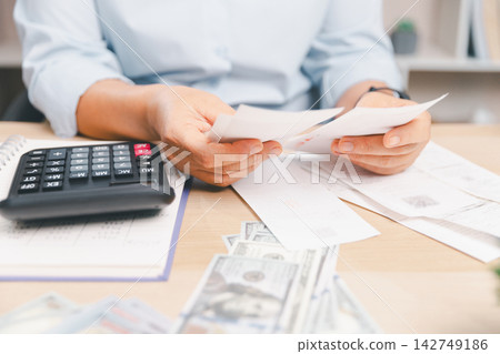 Person checking receipts and expenses beside a calculator and cash on a desk, illustrating budgeting, bills, debt, personal finance, household costs, accounting and financial planning. Person checking receipts and expenses beside a calculator and cash on a desk, illustrating budgeting, bills, debt, personal finance, household costs, accounting and financial planning. 142749186