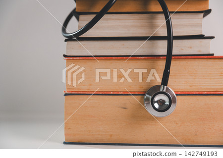 Close-up of a stethoscope hanging over a stack of books, representing medical education, healthcare learning, academic preparation, and study resources for future healthcare professionals. Close-up of a stethoscope hanging over a stack of books, representing medical education, healthcare learning, academic preparation, and study resources for future healthcare professionals. 142749193