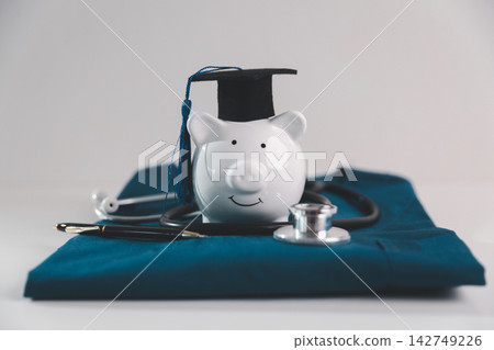 Piggy bank wearing a graduation cap with a stethoscope symbolizes medical education, career investment, student savings, healthcare training, tuition costs and financial planning. Piggy bank wearing a graduation cap with a stethoscope symbolizes medical education, career investment, student savings, healthcare training, tuition costs and financial planning. 142749226