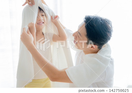 A father dries his child with a towel after their bath. 142750025