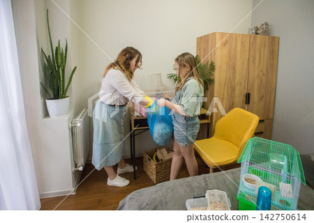 Mom and daughter work together to clean a pet hamster cage in a cozy room. Mom and daughter work together to clean a pet hamster cage in a cozy room. 142750614