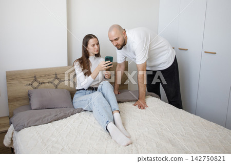 Nice woman holding smartphone and sitting with man in modern apartment watching video and relaxing. Nice woman holding smartphone and sitting with man in modern apartment watching video and relaxing. 142750821