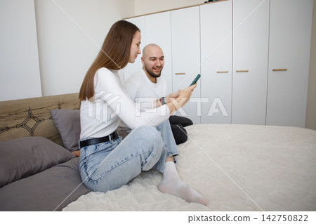 Cheerful woman holding smartphone and sitting with man in modern apartment watching video Cheerful woman holding smartphone and sitting with man in modern apartment watching video 142750822