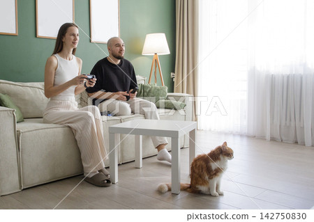 Smiling couple playing console game at home. Excited active pair video game Smiling couple playing console game at home. Excited active pair video game 142750830