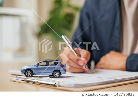 A man writes his signature on a car finance or lease agreement. Great for vehicle buying, renting, or dealership deals emphasizing auto loans A man writes his signature on a car finance or lease agreement. Great for vehicle buying, renting, or dealership deals emphasizing auto loans 142750922