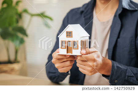 Real estate agent holds a miniature house model, representing property, finance, home loans, and housing concepts Real estate agent holds a miniature house model, representing property, finance, home loans, and housing concepts 142750929