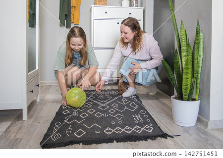 Mom and girl are in a living space focused on rolling a green ball with pet hamster. Mom and girl are in a living space focused on rolling a green ball with pet hamster. 142751451