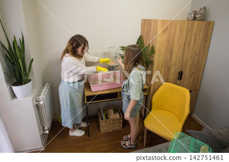 Two individuals stand in a room arranging small animal cages. Two individuals stand in a room arranging small animal cages. 142751461