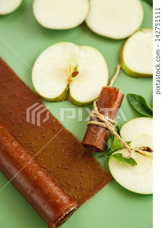 Natural dried apple puree rolls with slices on green background Natural dried apple puree rolls with slices on green background 142751511