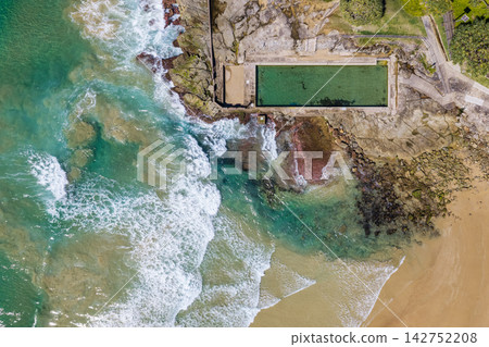 Downward aerial view of Yamba Main Beach and the ocean pool, showing the sandy shoreline, breaking waves and coastal swimming area beside the Pacific Ocean. Downward aerial view of Yamba Main Beach and the ocean pool, showing the sandy shoreline, breaking waves and coastal swimming area beside the Pacific Ocean. 142752208