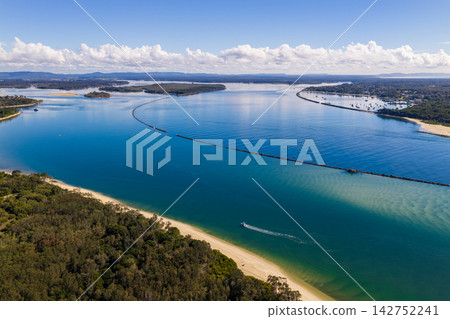Description: Aerial view of a boat creating a curved wake as it travels through the clear turquoise water of the Clarence River beside Whiting Beach at Yamba, New South Wales, Australia. Description: Aerial view of a boat creating a curved wake as it travels through the clear turquoise water of the Clarence River beside Whiting Beach at Yamba, New South Wales, Australia. 142752241
