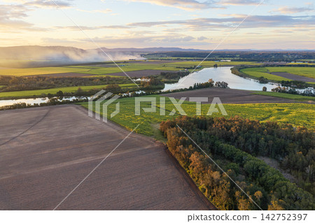 Aerial view over the Clarence River and surrounding farmland at sunset near Yamba, with smoke from a fire drifting across the distant rural landscape beneath a colourful evening sky Aerial view over the Clarence River and surrounding farmland at sunset near Yamba, with smoke from a fire drifting across the distant rural landscape beneath a colourful evening sky 142752397