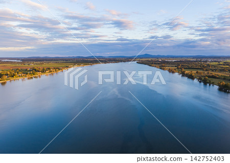 Aerial view over the expansive Clarence River and surrounding farmland near Yamba, showing the broad waterway winding through the rural landscape beneath a softly clouded sky Aerial view over the expansive Clarence River and surrounding farmland near Yamba, showing the broad waterway winding through the rural landscape beneath a softly clouded sky 142752403