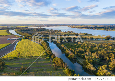 Aerial view over the expansive Clarence River and surrounding farmland near Yamba, showing the broad waterway winding through the rural landscape beneath a softly clouded sky Aerial view over the expansive Clarence River and surrounding farmland near Yamba, showing the broad waterway winding through the rural landscape beneath a softly clouded sky 142752408