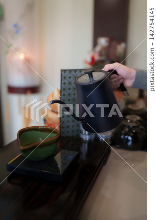 Hand pouring hot water from gooseneck kettle into green matcha bowl on digital scale in cafe with copy space Hand pouring hot water from gooseneck kettle into green matcha bowl on digital scale in cafe with copy space 142754145