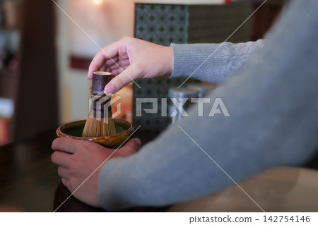 Hands whisking matcha powder in ceramic bowl using traditional bamboo chasen during tea preparation ceremony Hands whisking matcha powder in ceramic bowl using traditional bamboo chasen during tea preparation ceremony 142754146