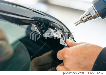 A car wrapping specialist applies a polyurethane film to the car. Detailer PPF A car wrapping specialist applies a polyurethane film to the car. Detailer PPF 142754237