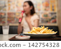 A woman enjoying karaoke with a plate of french fries on the table. 142754328