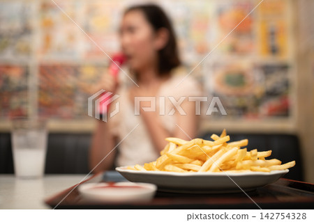 一位女士正在欣賞卡拉OK，桌上放著一盤薯條。 142754328