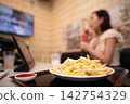 A woman enjoying karaoke with a plate of french fries on the table. 142754329