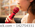 A close-up of a woman's mouth as she passionately sings into a red microphone at karaoke. 142754331