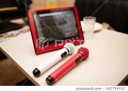 卡拉OK包廂的桌子上放著兩個麥克風和一個點歌平板電腦。 卡拉OK包廂的桌子上放著兩個麥克風和一個點歌平板電腦。 142754332