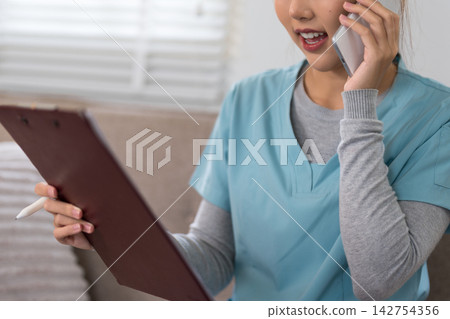 Young Asian female healthcare professional talking on phone while reviewing patient chart on tablet in bright clinic Young Asian female healthcare professional talking on phone while reviewing patient chart on tablet in bright clinic 142754356