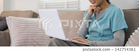 Asian female doctor smiling while using laptop computer on sofa in modern clinic with copy space Asian female doctor smiling while using laptop computer on sofa in modern clinic with copy space 142754361
