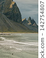Surfer in the waves at Stokksnes beach with Vestrahorn mountains in the background, South East Iceland 142754807