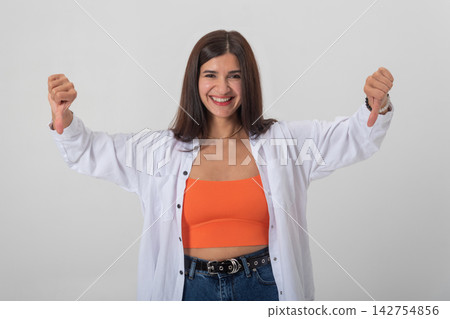 Young woman smiling while showing two thumbs down signs to express disapproval, rejection or negative feedback on a clean white background, casual studio portrait emotion Young woman smiling while showing two thumbs down signs to express disapproval, rejection or negative feedback on a clean white background, casual studio portrait emotion 142754856