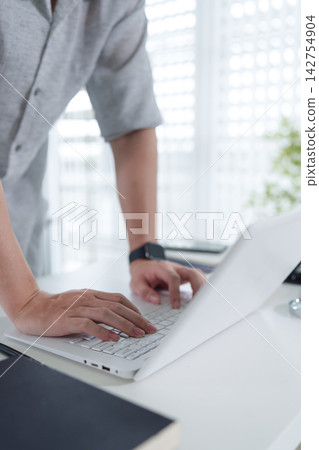 Asian businesswoman in gray suit typing on laptop computer at modern urban office desk with city view Asian businesswoman in gray suit typing on laptop computer at modern urban office desk with city view 142754904