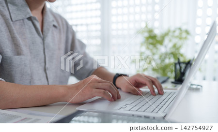Asian professional woman typing on laptop at bright modern office desk with city view and copy space Asian professional woman typing on laptop at bright modern office desk with city view and copy space 142754927