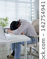 Exhausted Asian man experiencing burnout while working from home with laptop at modern office desk 142754941
