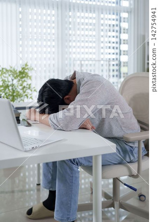 Exhausted Asian man experiencing burnout while working from home with laptop at modern office desk Exhausted Asian man experiencing burnout while working from home with laptop at modern office desk 142754941