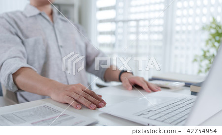 Asian professional typing on laptop at modern home office desk with documents and natural lighting Asian professional typing on laptop at modern home office desk with documents and natural lighting 142754954