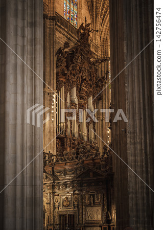 Baroque pipe organ with carved angels seen between gothic columns in Seville Cathedral 142756474