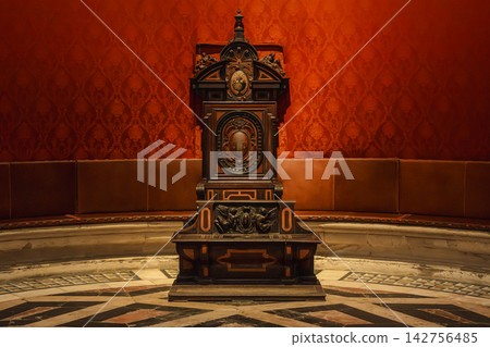 Elliptical domed chapter house of Seville Cathedral with red damask walls and archbishop's throne 142756485