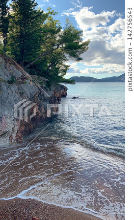 Rocky cliffside meets calm azure sea at shoreline during sunset with dramatic clouds rolling over Adriatic mountains under golden light illuminating forest greenery Rocky cliffside meets calm azure sea at shoreline during sunset with dramatic clouds rolling over Adriatic mountains under golden light illuminating forest greenery 142756543