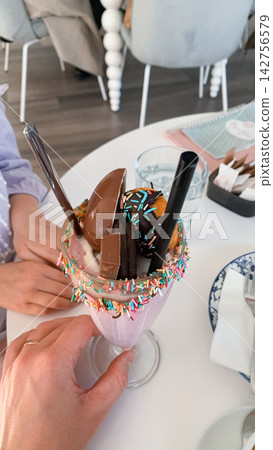 Close up of hands holding a giant decorative milkshake filled with cookies and candies at a table Close up of hands holding a giant decorative milkshake filled with cookies and candies at a table 142756579