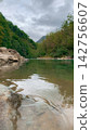 Low angle closeup of calm emerald river water flowing over smooth stones in a deep green forest 142756607