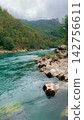 Emerald stream carving through a deep mountain valley with scattered stone formations and lush forest backdrop under a soft grey sky reflecting the untouched beauty of a natural water course 142756611