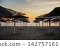 Rows of Straw Beach Umbrellas on Empty Beach at Sunset 142757161