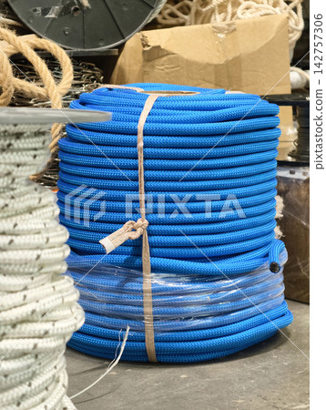Thick blue rope in a large tight coil showing high strength braided fiber material suitable for lifting fastening and general utility tasks in construction and logistics work Thick blue rope in a large tight coil showing high strength braided fiber material suitable for lifting fastening and general utility tasks in construction and logistics work 142757306