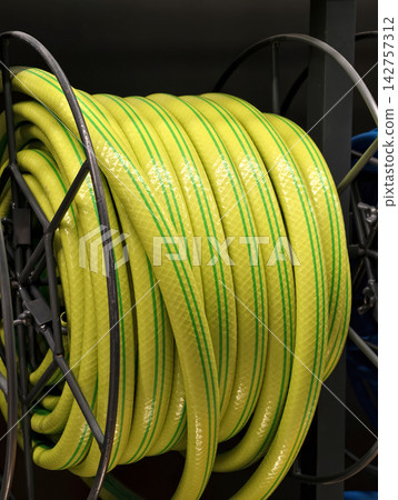 Yellow hose with green stripes coiled neatly is displayed on store shelves for watering gardens and other household uses Yellow hose with green stripes coiled neatly is displayed on store shelves for watering gardens and other household uses 142757312