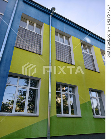 Updated school facade painted in blue yellow and green tones with modern replacement windows Updated school facade painted in blue yellow and green tones with modern replacement windows 142757317
