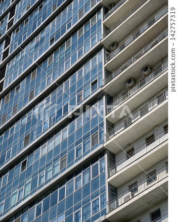 Tall blue residential tower with modern balconies and countless apartment windows in urban surrounding Tall blue residential tower with modern balconies and countless apartment windows in urban surrounding 142757319
