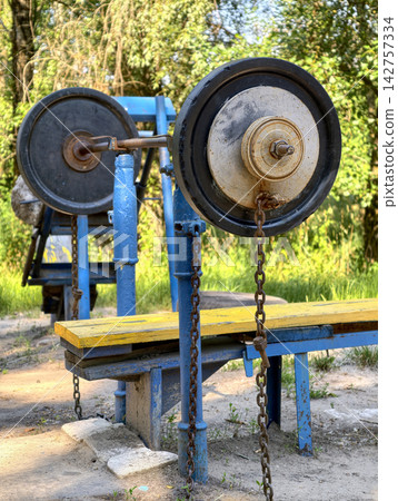 Loaded barbell with rubber and iron weight plates placed on a yellow horizontal bench at a shared outdoor gym area for chest training and muscle development Loaded barbell with rubber and iron weight plates placed on a yellow horizontal bench at a shared outdoor gym area for chest training and muscle development 142757334