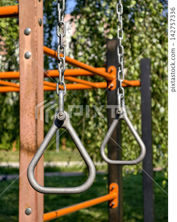 Triangular hanging handles attached to chains on an outdoor fitness area for bodyweight exercises, grip training and upper body workouts Triangular hanging handles attached to chains on an outdoor fitness area for bodyweight exercises, grip training and upper body workouts 142757336